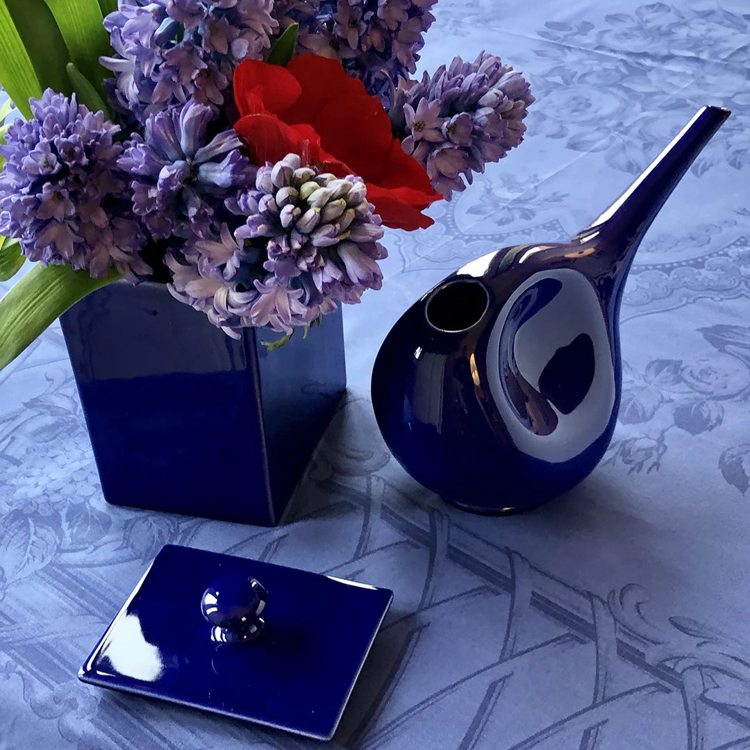 Blaue Gießkanne mit Blumen auf einem gedeckten Tisch